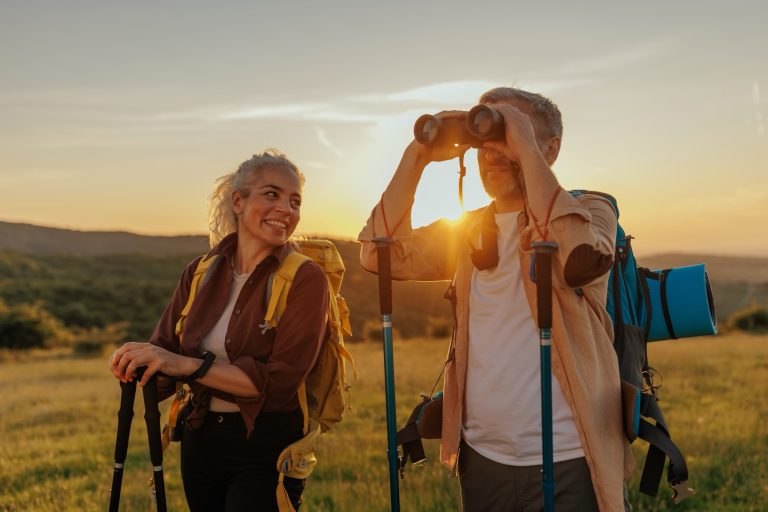 Retired couple hiking together at sunset, looking through binoculars